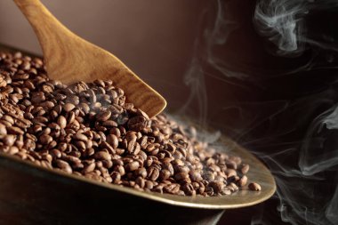 Orta pişmiş kahve çekirdekleri kızartma tavasında dumanlıdır. Boşluğu kopyala.