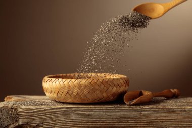 Chia tohumları hasır bir kaseye dökülür. Kopyalama için arkaplan.