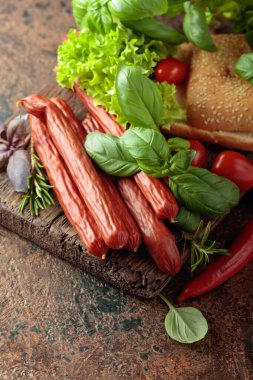 İnce tütsülenmiş sosisler, eski bir kesim tahtasının üzerinde ekmek ve yeşillikler..