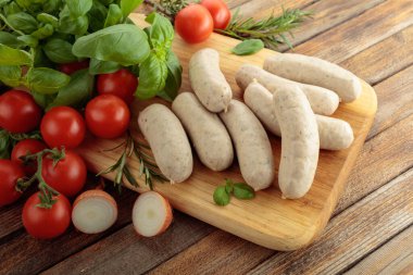 Geleneksel Bavyera beyaz sosisleri fesleğen ve domatesli ahşap kesim tahtasında.