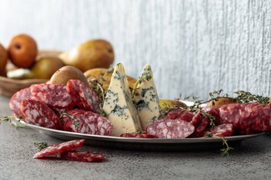 Mavi peynir, kurutulmuş sosis, kekik ve armut gri bir taş masada..