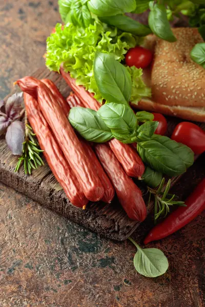 İnce tütsülenmiş sosisler, eski bir kesim tahtasının üzerinde ekmek ve yeşillikler..