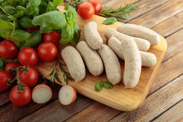 Geleneksel Bavyera beyaz sosisleri fesleğen ve domatesli ahşap kesim tahtasında.