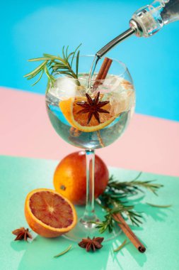 Cin, tonik, kan portakalı, tarçın, anason ve biberiyeli yaz kokteyli. Buzda servis ediliyor, renk ve tazelikle dolup taşıyor. Parlak renkli arkaplan.
