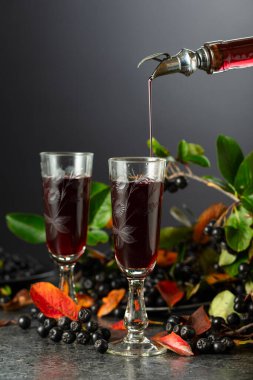 Böğürtlen suyu şişeden bardağa dökülür. Tatlı içecek ve taze böğürtlen siyah bir taş masada..