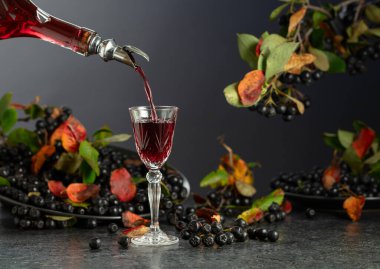 Siyah böğürtlen likörü ve siyah taş bir masada taze böğürtlen. Tatlı aromalı içecek şişeden bardağa dökülür..