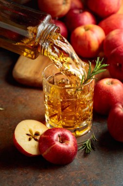 Elma suyu şişeden bardağa dökülür. Bir bardak meyve suyu ve taze elma eski bir mutfak masasında oturuyor..