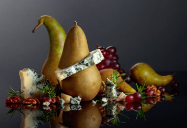 Armut, ceviz, kırmızı üzüm ve biberiyeli mavi peynir. Siyah yansıtıcı arka planda meyveleri olan geleneksel küflü peynir. Boşluğu kopyala.