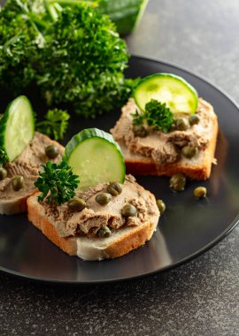 Pate, taze salatalık, kapari ve maydanozlu sandviç. Siyah tabakta ezmeli tost..
