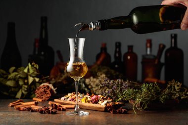 Bitkisel merhem eski bir şişeden bardağa dökülür. Kurutulmuş otlar, çiçekler, baharatlar ve eski mutfak aletleri. Bitkisel ilaç kavramı.