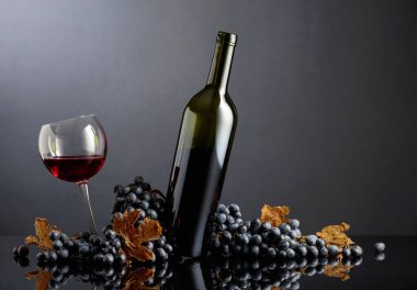 Siyah arka planda mavi üzümlü bir şişe ve bir bardak kırmızı şarap. Boşluğu kopyala.