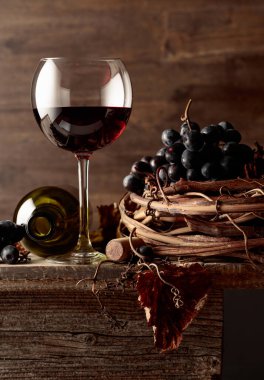 Eski ahşap bir masada üzümlü bir bardak ve bir şişe kırmızı şarap..