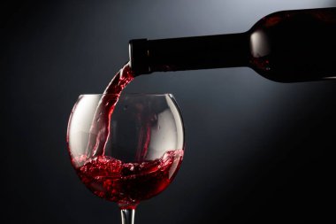 Kırmızı şarabı siyah arka planda bir şarap bardağına döküyorum..