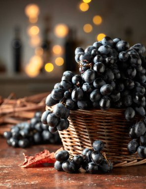 Kahverengi bir masada eski sepetteki mavi üzümler. Arka plandaki tezgahta çeşitli şarap şişeleriyle. Önplana odaklan.
