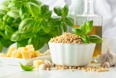 Malzemeli pesto sosu. Fesleğen, çam fıstığı, sarımsak, parmesan ve beyaz ahşap bir masada zeytin yağı. Geleneksel İtalyan pesto tarifi.