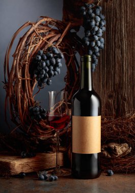 Kurumuş asma ve mavi üzümlerin olduğu eski bir tahtanın arka planına karşı şişe ve bir bardak şarap. Şişede mesajın için yeri olan eski bir etiket var. Yıllanmış şarap konsepti.