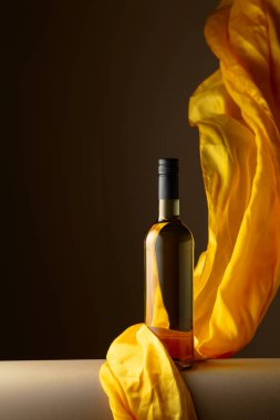 Bir şişe beyaz şarap ve koyu bir arka planda çırpınan sarı kumaş..