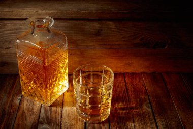 Zarif viski bardağı ve kehribar sıvısıyla dolu sürahi eski bir ahşap masada. Boşluğu kopyala.