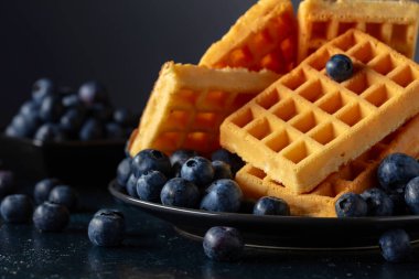 Siyah tabakta taze yaban mersinli Belçika waffleları. Koyu mavi bir masada waffle ve taze böğürtlen.