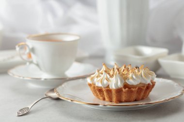 Beyaz bir masada kremalı turta. Kremalı turta, bir fincan çay ve beyaz mermer tezgahta beyaz mutfak aletleri..
