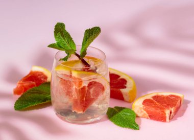 Buzlu, greyfurtlu ve nane şekerli yaz içeceği. Serin, gevrek ve pembe bir arka planda palmiye gölgeleri tarafından öpülmüş. Boşluğu kopyala.