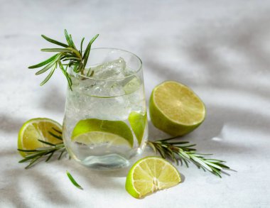 Buzlu, limonlu ve biberiyeli ferahlatıcı bir yaz içeceği. Serin ve ferahlatıcı bir içecek, mermer bir masanın üzerinde palmiye gölgeleri. Boşluğu kopyala.