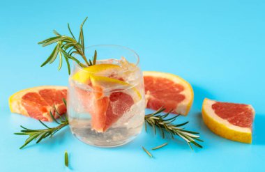 Buzlu, pembe greyfurtlu ve biberiyeli yaz ferahlatıcı içecek. Kopyalama alanı olan mavi arkaplan.