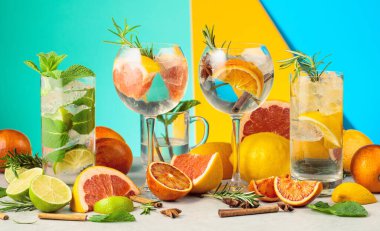 Beyaz mermer bir masada malzemelerle yaz kokteyllerini tazeliyorum. Mojito ve çeşitli cin tonik kokteylleri parlak renkli bir arka planda..