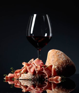 Ciabatta soslu jambon, kırmızı şarap ve siyah yansıtıcı arka planda kekik.. 