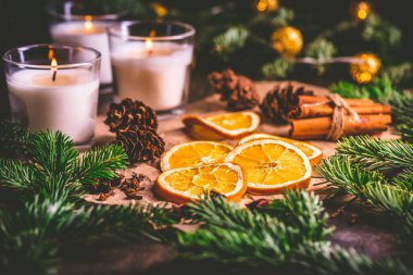 Kurumuş portakal ve Noel baharatları, noel ağacı dalları, tarçın, mutfak masasında mumlar.