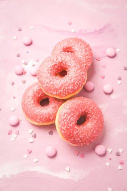 Pembe donutlar ve pembe arka planda pembe çikolata taneleri.