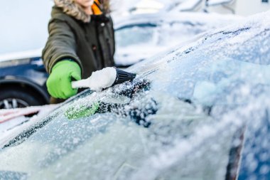 Teenager  cleans car after a snowfall, removing snow and scraping ice  