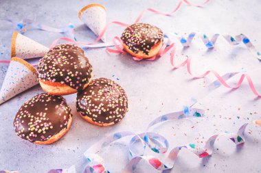 Chocolate Berliner pastry for carnival and party. German Krapfen or donuts with streamers and confetti.  Colorful carnival or birthday image