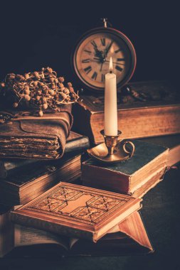 Old antique books with candle and vintage clock on wooden background