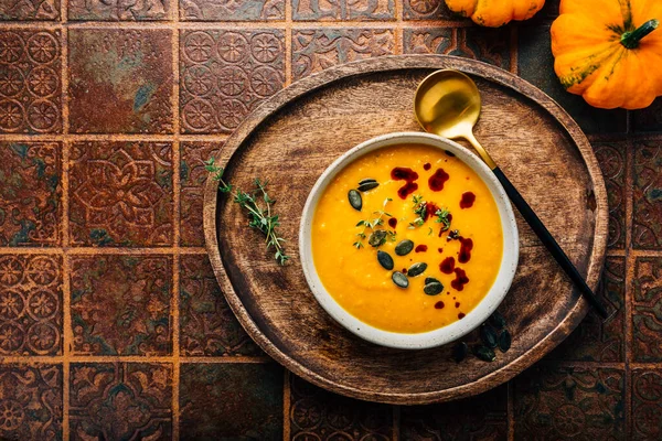 Pumpkin soup with pumpkin seeds  and pumpkin seed oil served in bowl on rustic kitchen table