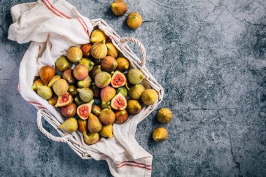 Gri arka planda sepetten taze toplanmış organik yeşil incirler.