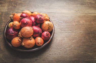 Ahşap mutfak masasındaki kasede kırmızı ve sarı soğanlar.