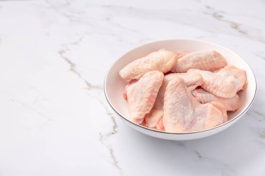 Beyaz kasede çiğ tavuk kanadı, mermer arka planda pişmeye hazır.