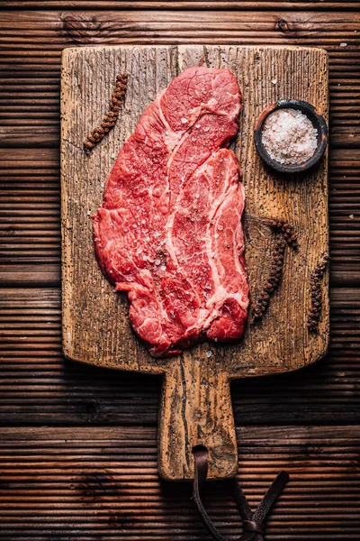 Raw Chuck eye beef steak seasoned with salt and pepper on wooden cutting board