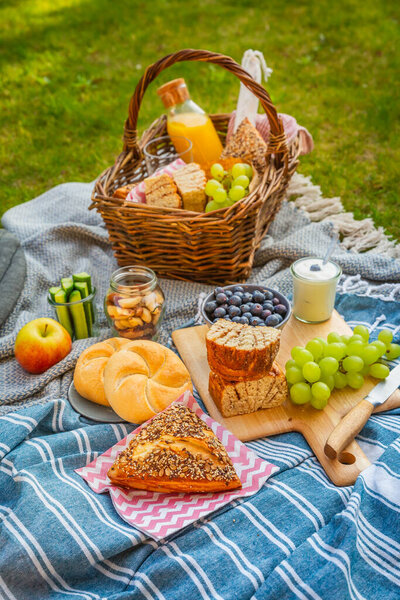 Picnic duvet and basket with different food, fruits, orange juice., yogurt and bread on green grass