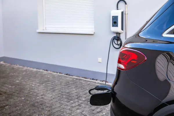 stock image Generic electric vehicle EV hybrid car is being charged from a wallbox on a contemporary modern residential building house