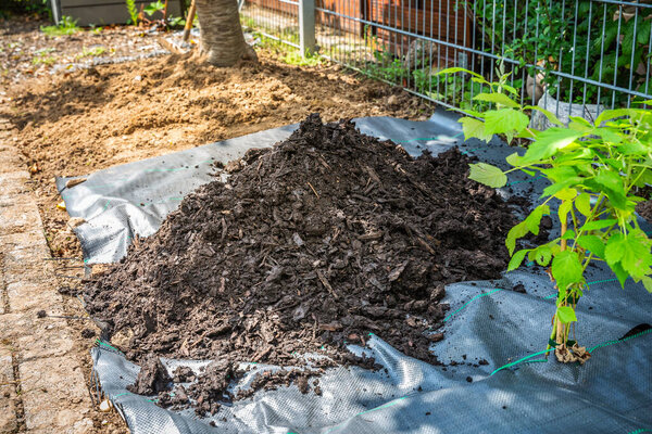 Installing weed control fabric material and bark mulch in a residential garden to control weed spreading
