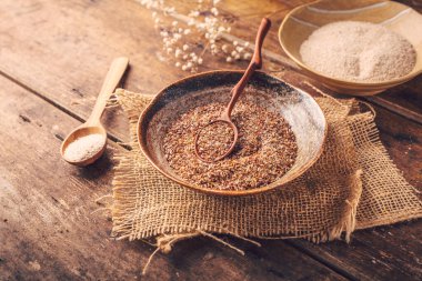 Tahta bir masada parçalanmış keten tohumu ve Psyllium kabuğu (Isabgol) yığını.