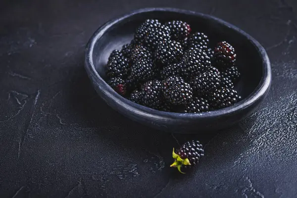 Bahçeden yeni toplanmış organik böğürtlenler siyah arka planda bir kasede