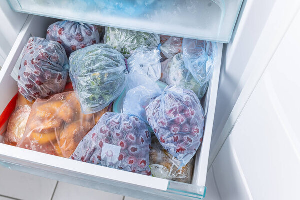 Замороженные фрукты и овощи в пластиковых пакетах в морозильнике без мороза, бытовая концепция