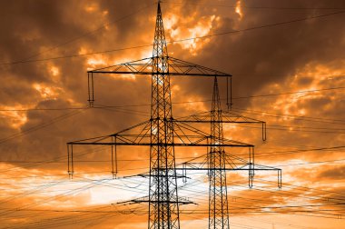 high voltage pylons for electricity and power against sky with dramatic clouds clipart
