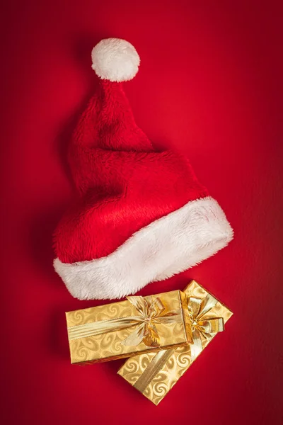 Χρυσό Χριστουγεννιάτικο Δώρο Και Κόκκινο Καπέλο Σάντα Στο Κόκκινο Φόντο — Φωτογραφία Αρχείου