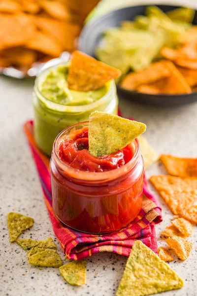 Red and green salsa with tortilla chips on the kitchen table.