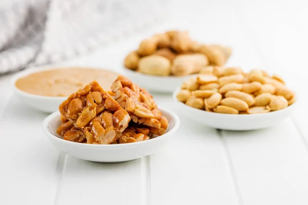 Sweet peanut brittle, peanuts and peanuts butter on the white table.