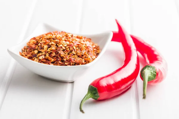 Dry chili pepper flakes. Crushed red peppers in bowl on the white table.